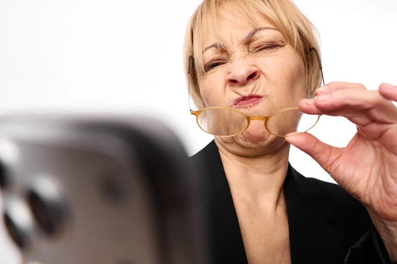 Elderly woman in studio closeup, creating a soap bubble near lips, eyes closed and playful expression, black clothing, clean white background, soft light, gentle air