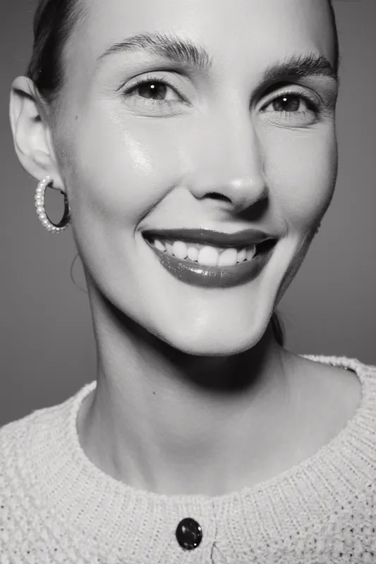 Closeup of smiling Caucasian woman with fair skin in sweater and hoop earrings. Bright studio lighting highlights natural beauty and positive cheerful mood.