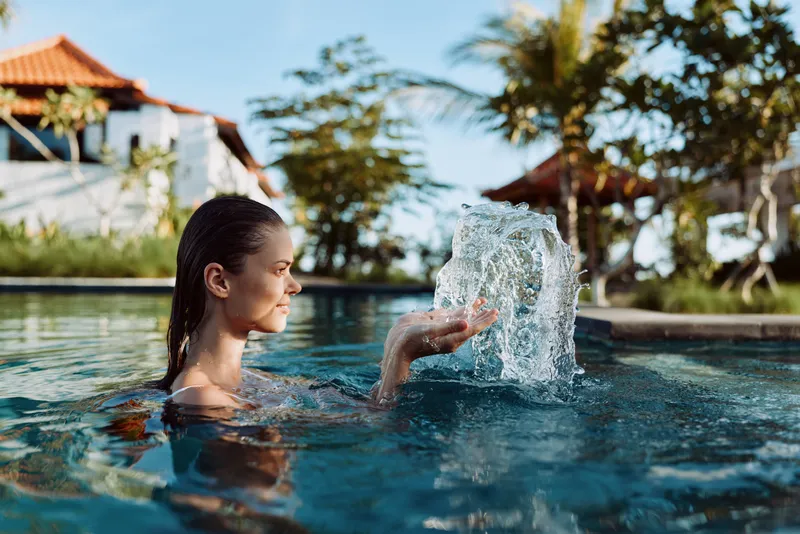 A woman enjoys a refreshing splash in a sunny pool, capturing a relaxed lifestyle moment outdoors at a tropical resort, playful water and calm mood.