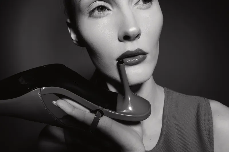 Portrait of pale white woman holding black high heel shoe near face, black and white photo with dramatic lighting and elegant style concept.
