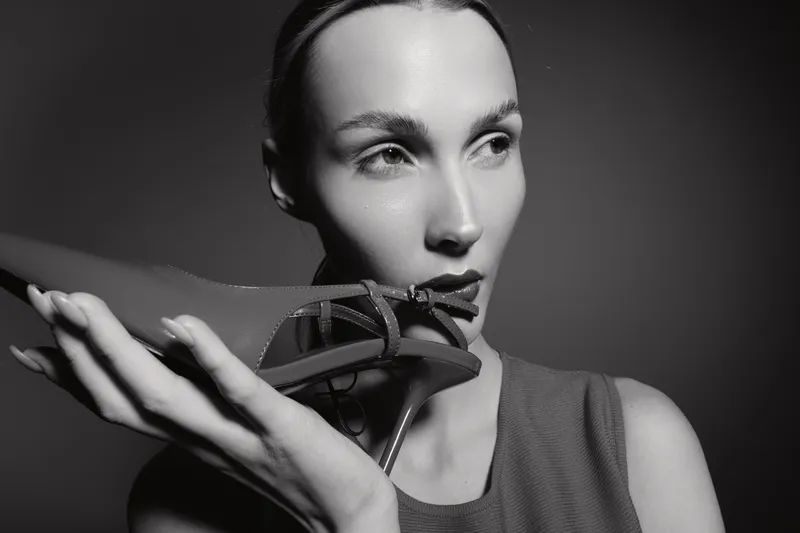 Close-up of a fair skinned Caucasian woman holding a high heel shoe near her face in black and white. Concept of fashion and style with elegant mood.