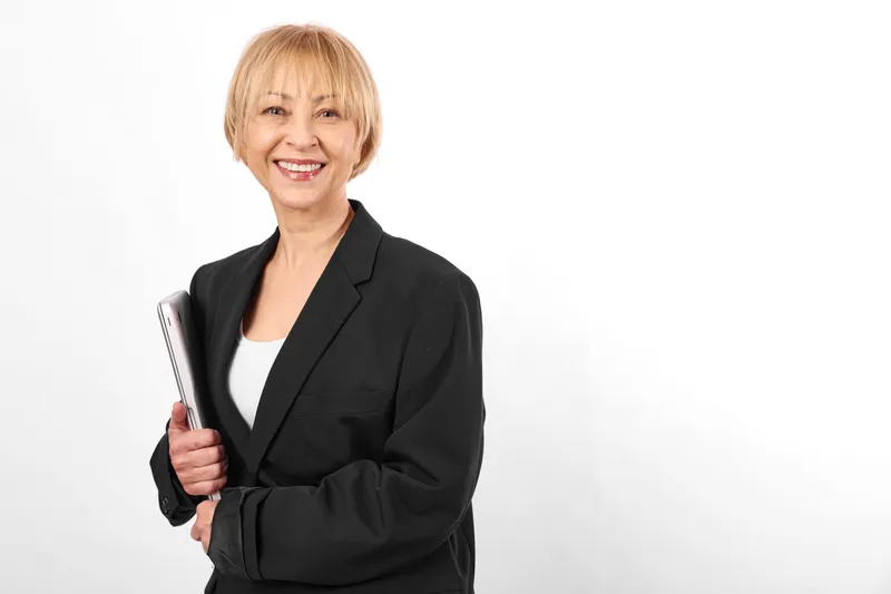 Smiling mature businesswoman in a black suit holds a tablet in a studio portrait on a clean white background, professional corporate communication concept, confident business