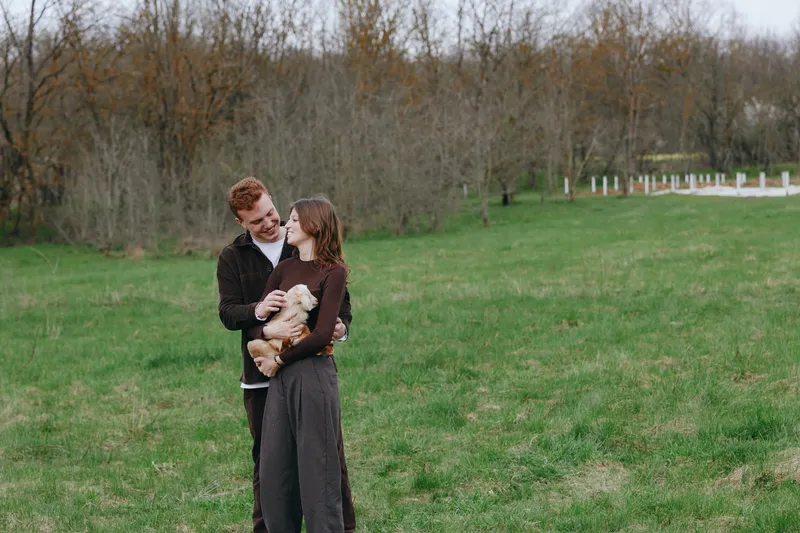 Couple outdoors lifestyle in a field of green countryside, happiness shown as they cradle a goat kid, animals blending with nature in a warm candid moment