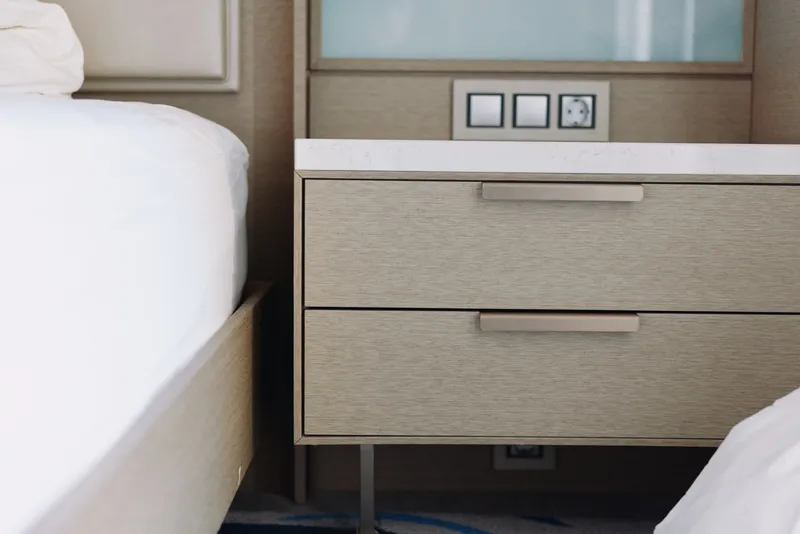 Bedside table with two drawers beside a bed in a bedroom. Clean lines, neutral tones and warm wood finish convey a calm, organized living space.