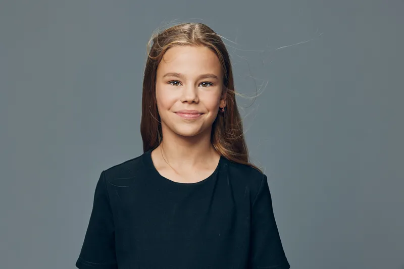 Girl portrait with long hair and smile against gray background wearing black shirt in studio setting for child, youth and innocence concept with natural expression and casual style.