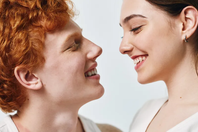 Young man and woman smiling face to face in closeup with happy expressions and positive emotions on light background. People, love and friendship portrait.