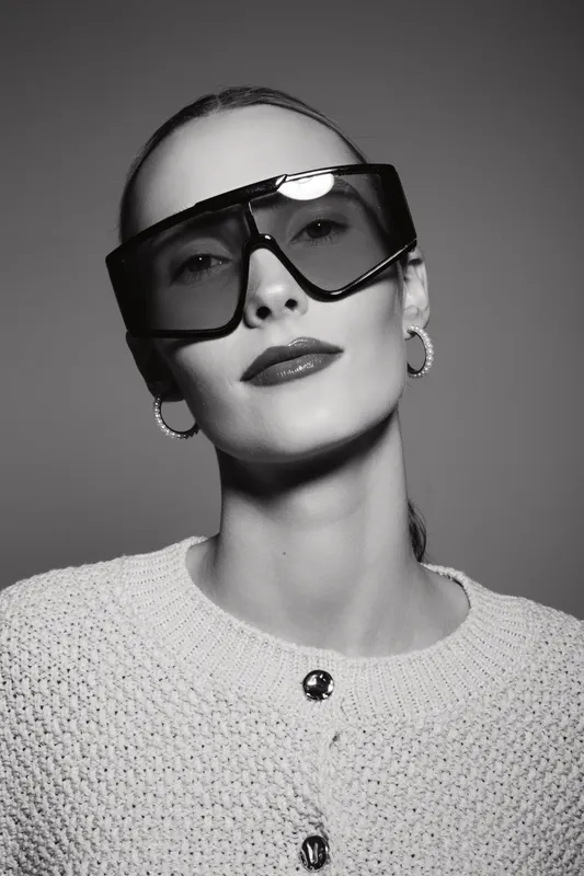 Portrait of a light skinned caucasian woman wearing large sunglasses and hoop earrings in studio gray background.