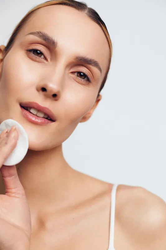 Young woman skincare routine close up she holds cotton pad on cheek gentle cleansing on clean light background fresh natural beauty look at home calm expression makeup free hygiene spa mood
