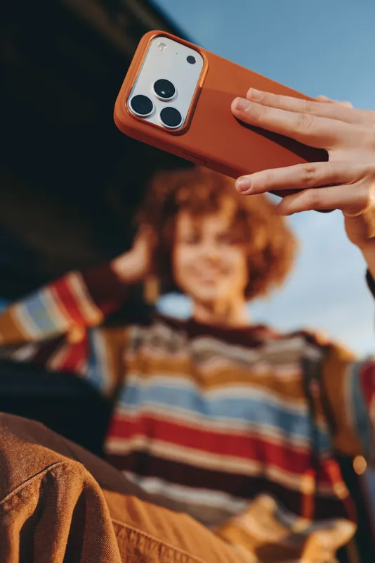 Woman hand holding smartphone in living room, lifestyle moment, casual communication, blurred child on home couch, cozy warm lighting, relaxed family indoors, everyday media sharing