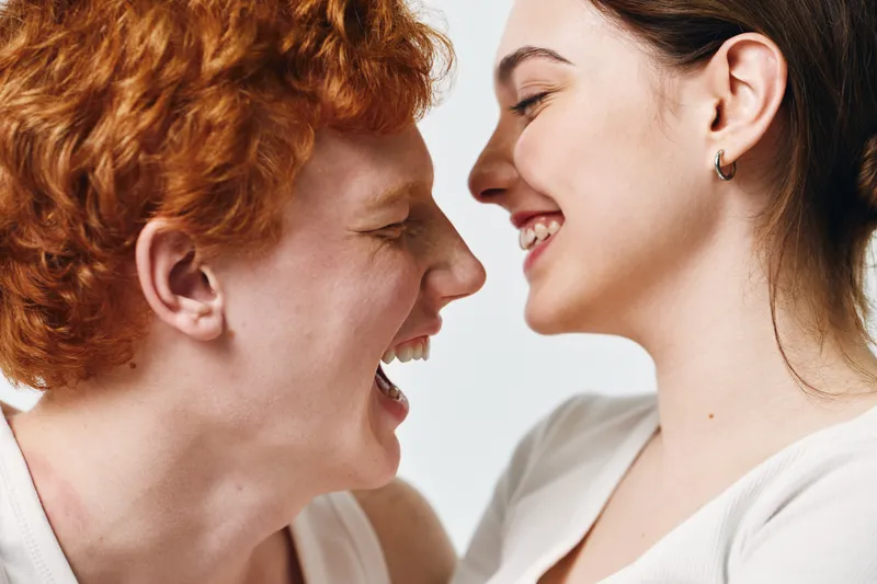 Happy young couple smiling and facing each other with joy and affection. Closeup portrait of two people expressing love and positive emotions in casual clothing.