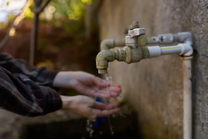 Close-up of hands under a running tap outdoors, washing under cool water, focusing on hygiene, cleanliness, and daily rituals in a natural setting
