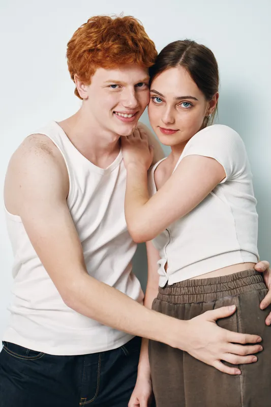 Young couple, man and woman in casual clothes posing together with affection and smile on white background, showing close connection and relaxed mood at studio portrait.