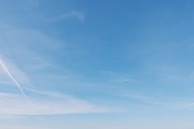Sky with blue tones and clouds and contrails across the horizon, daylight mood, serene and expansive atmosphere ideal for travel, aviation and nature themed stock.