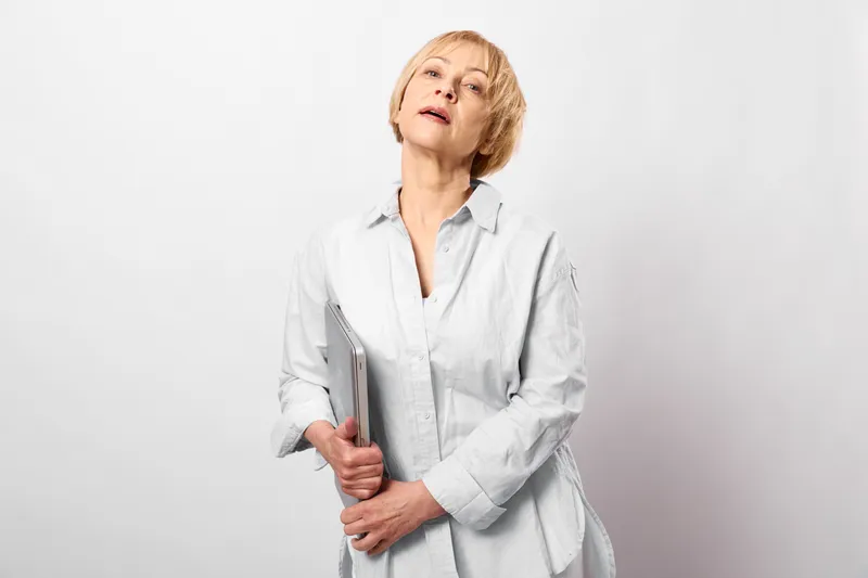Woman doctor nurse holding clipboard, portrait in white studio background, serious expression, medical professional standing, health caregiver role, clean soft neutral colors