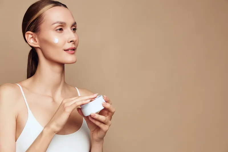 Skincare moment with a woman applying cream, soft natural lighting, calm expression, minimalist backdrop, hydrated skin, subtle glow, clean composition, everyday beauty