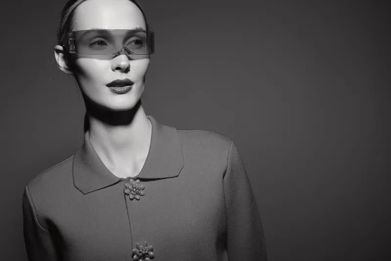 Stylish Caucasian woman with pale skin wearing large sunglasses and a textured jacket against dark background. Concept for fashion, elegance, and modern style.