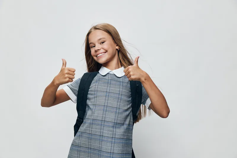 Girl child with backpack smiling and showing thumbs up gesture for school, education and positive attitude in studio. Happy kid with long hair and casual clothes on white background