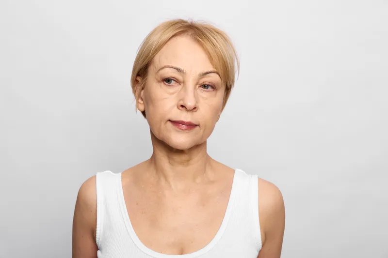 Elderly woman portrait neutral short hair white sleeveless gray background in studio headshot showing calm mature face with soft light and subtle wrinkles for age retirement