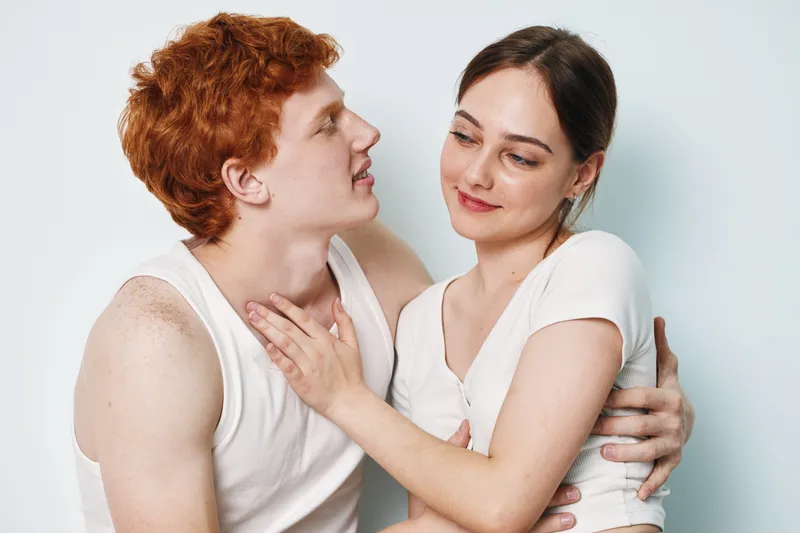 Couple, young man and woman in casual white tops, embracing and looking at each other lovingly, portrait of romantic relationship and close connection with gentle expression.