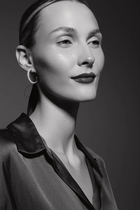 Elegant white woman with light skin poses in black and white portrait wearing silk blouse and hoop earrings.