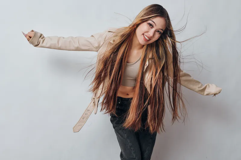 Young woman with long hair and casual clothes smiling and posing with open arms on gray background for lifestyle and fashion portrait.