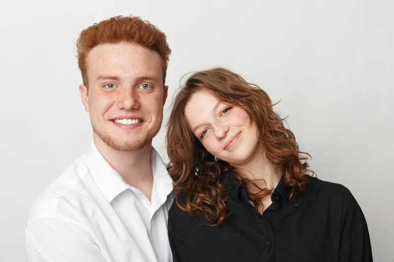Smiling young man and woman with curly hair pose together against white background. Casual clothing and friendly expressions create warm, positive mood of friendship and connection.