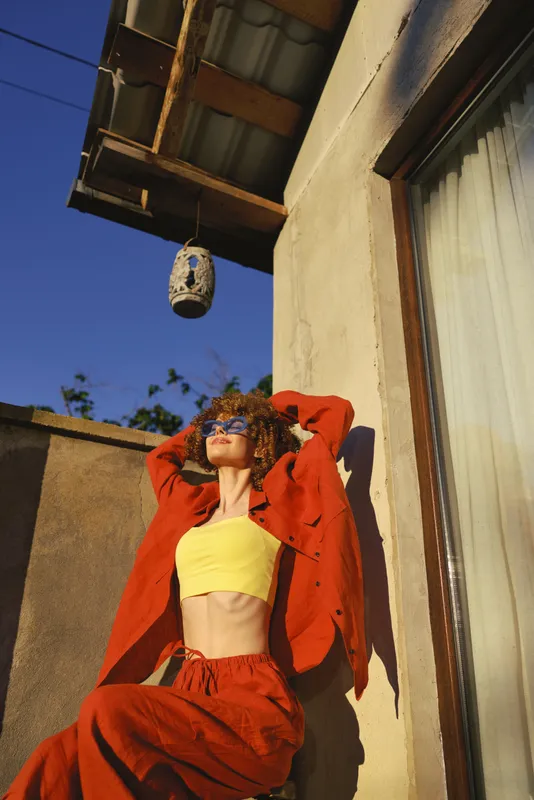 Vibrant woman lifestyle outdoor in bold red suit and yellow crop top, posing confidently against a sunny urban wall for a colorful fashion moment
