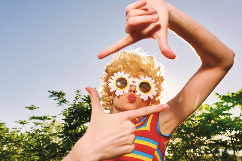 Cheerful child outdoors, playful frame moment, sunlit scene, colorful striped outfit, retro film color, vibrant greenery background, candid joy