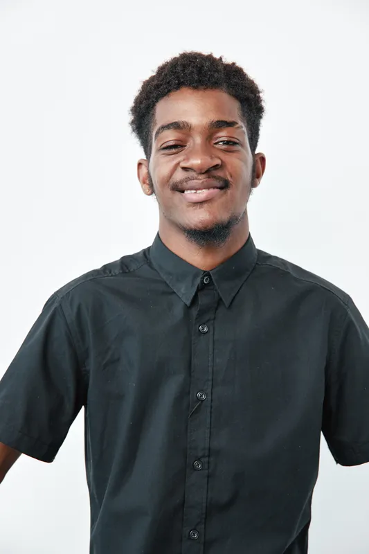 Young African American man with dark skin and curly hair wearing black shirt smiling with closed eyes on white background in studio portrait.