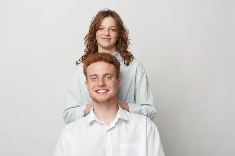 Smiling young man and woman with casual clothes pose together on light background. Friendly couple with natural expressions shows positive mood and relaxed lifestyle concept.