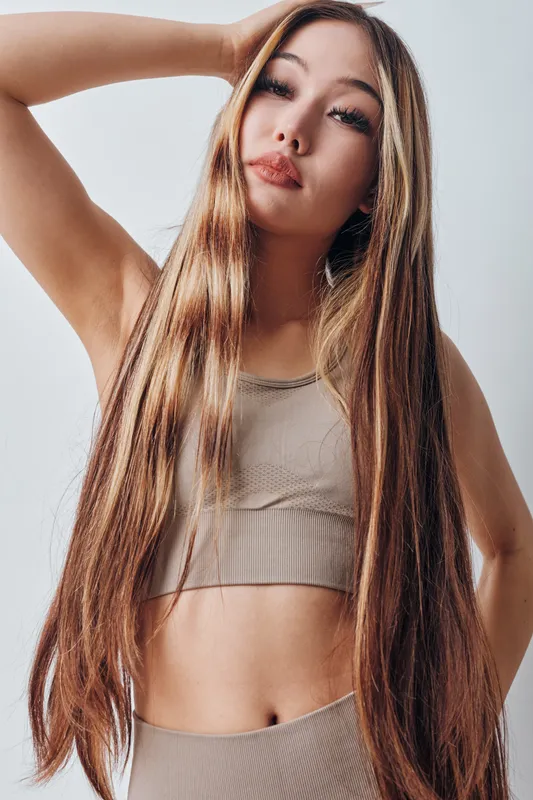 Woman with long straight hair posing in casual sportswear top against plain light background for beauty fashion lifestyle and confidence portrait.