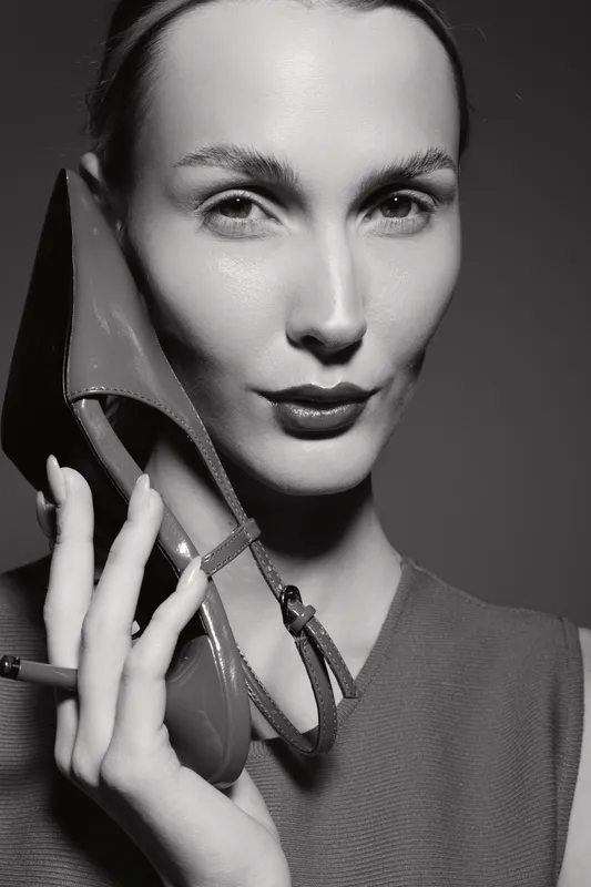 Portrait of a caucasian woman with light skin holding a high heel shoe near her face in black and white. Fashion concept with elegant female model.