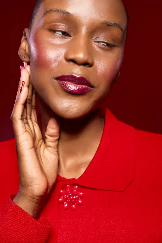 Close-up of a smiling black woman with dark skin wearing a red sweater with floral detail, posing against a red background. Concept of beauty, fashion, confidence, and elegance.
