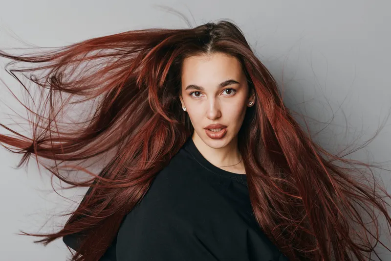 Woman with long red hair flowing and wearing black shirt posing on grey background. Portrait of young female with expressive face and natural makeup in studio lighting.
