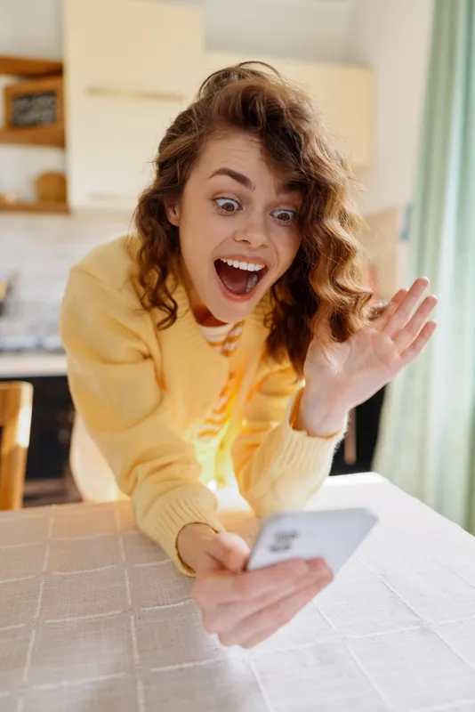 Cheerful woman indoors at home, taking a selfie with bright natural light, casual outfit, joyful expression, cozy living space, soft colors, candid lifestyle moment