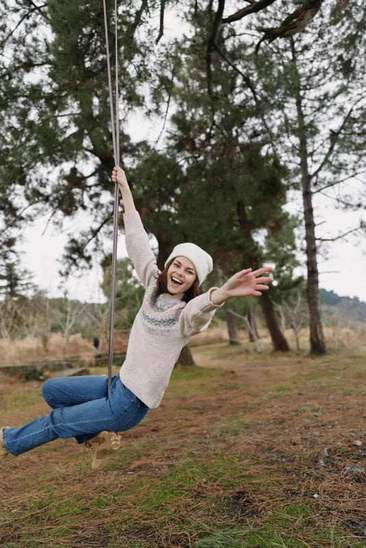 Woman on a swing in an outdoor park, smiling and carefree, enjoying nature and fresh air during a relaxed, joyful moment amid trees.