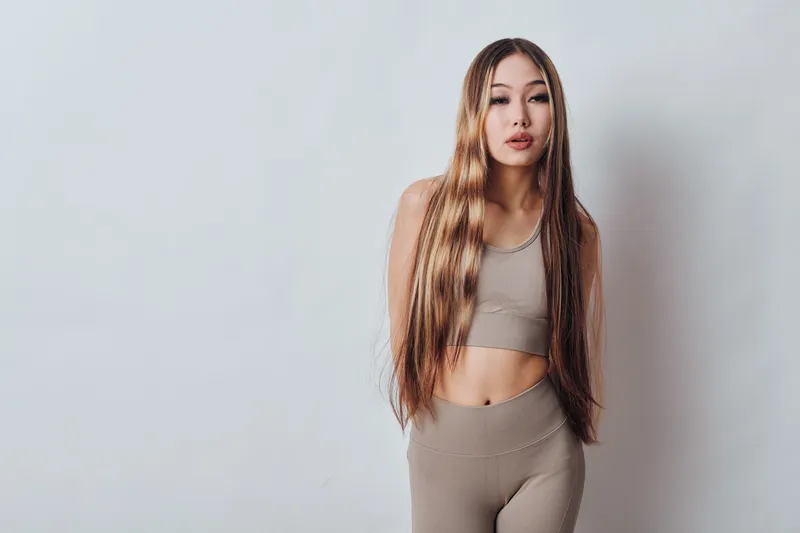 Woman with long braided hair poses in beige crop top and leggings against white background, fashion portrait, beauty style and confident young female model indoor.