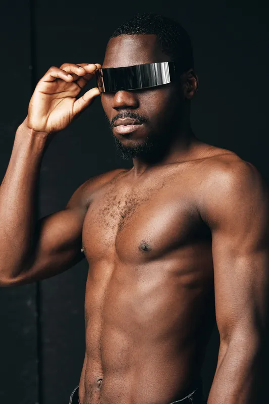 African man shirtless with futuristic visor glasses in creative conceptual visual style. Dark skin, muscular body, modern technology, fashion and innovation in studio portrait.