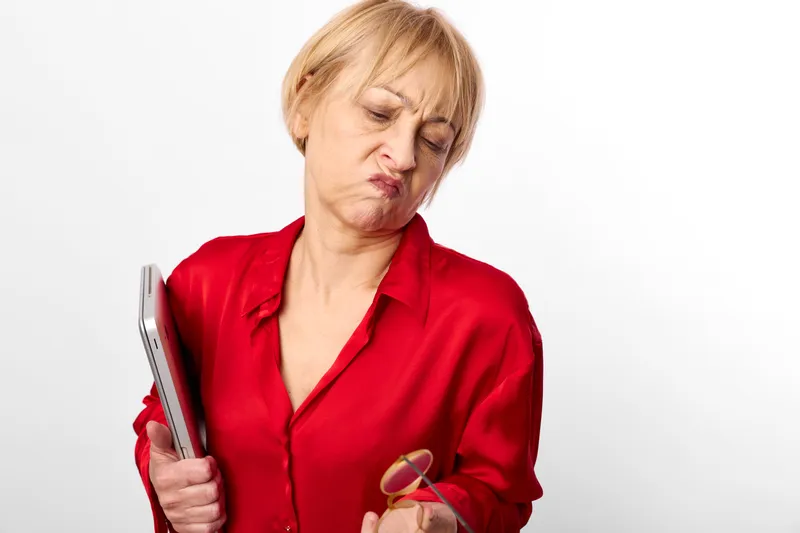 Elderly woman in red blouse holding a smartphone and candy, showing nausea and pain expression, white studio background, concept of health care, communication through technology, home wellbeing
