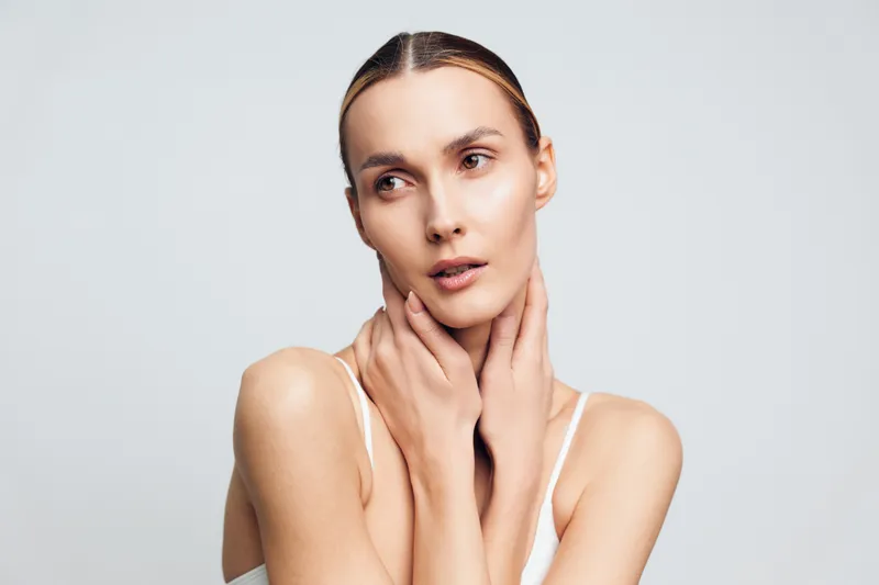 Woman skincare portrait, young beauty model in studio, hands on face, calm expression, soft diffused light, clean white background, minimal styling, gentle skin care