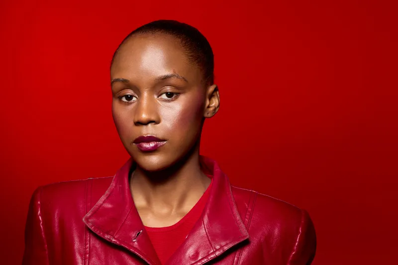 Portrait of a confident black woman with dark skin wearing a red leather jacket against a vibrant red background. Concept of fashion, empowerment, and bold style.