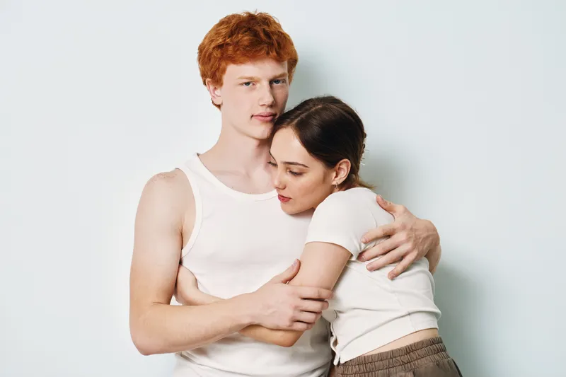 Couple hugging with affection and closeness, young man and woman embracing each other, tenderness and comfort in casual clothes against plain background.