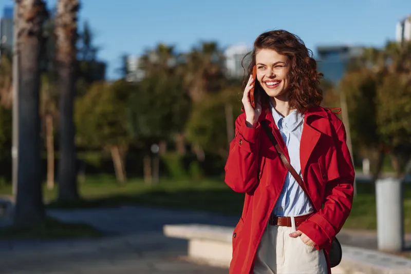 Smiling woman in a red coat outdoors, sunny day, casual chic fashion, candid portrait, bright mood, soft natural light, highlights expression and confident style.
