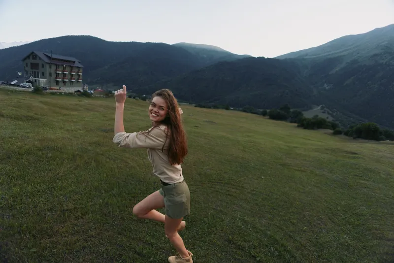 Happy woman outdoors posing on green grass field with mountains in background casual outfit natural light smiling joyful lifestyle summer day