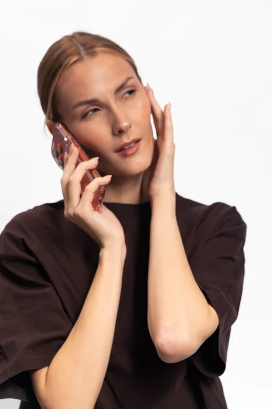 Young woman with smartphone in hand talks and looks away thinking. Casual style, natural light on white background. Concept of communication, technology, and lifestyle.