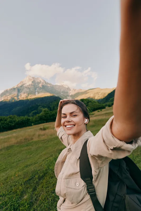 Smiling woman with a backpack hiking outdoors in a sunny meadow with distant mountains, conveying wellness and adventure, in bright light enjoying fresh air and freedom