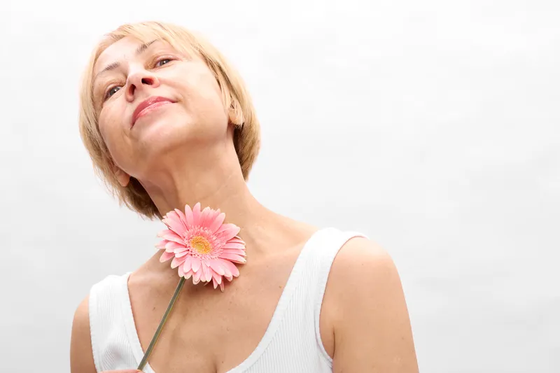 Woman portrait flower gerbera blonde isolated on white studio background, woman poses with pink gerbera on neck, soft beauty smile, closeup shot for skincare