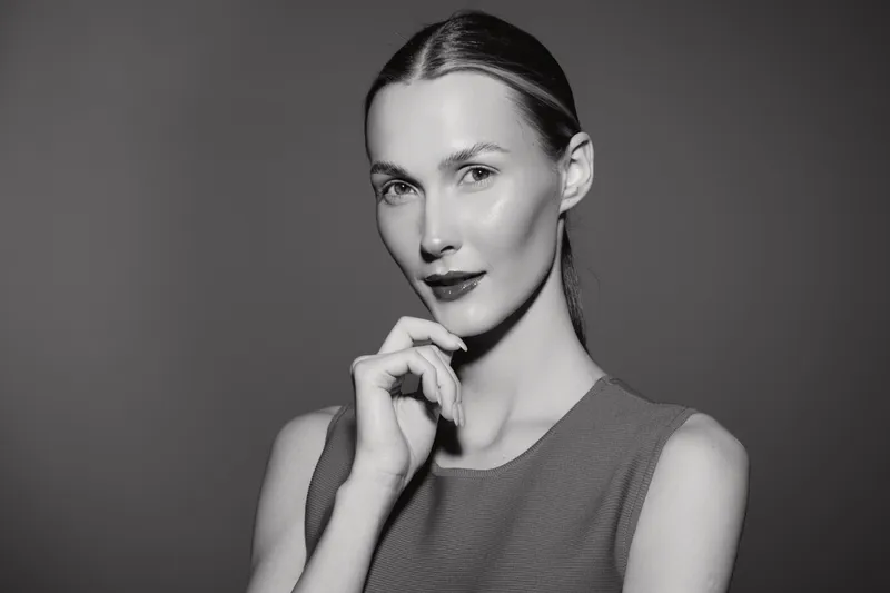 Portrait of a confident white woman with light skin and slicked back hair posing thoughtfully against a plain background in studio lighting. Concept for beauty and confidence.