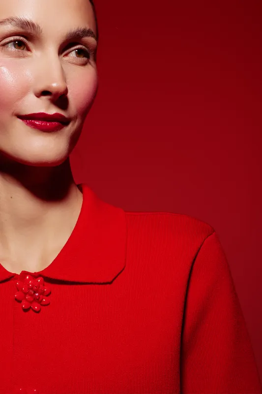 Close-up of a smiling woman with clear skin wearing red lipstick and a red top against a red background. Concept of beauty, fashion, makeup, and confident female portrait.