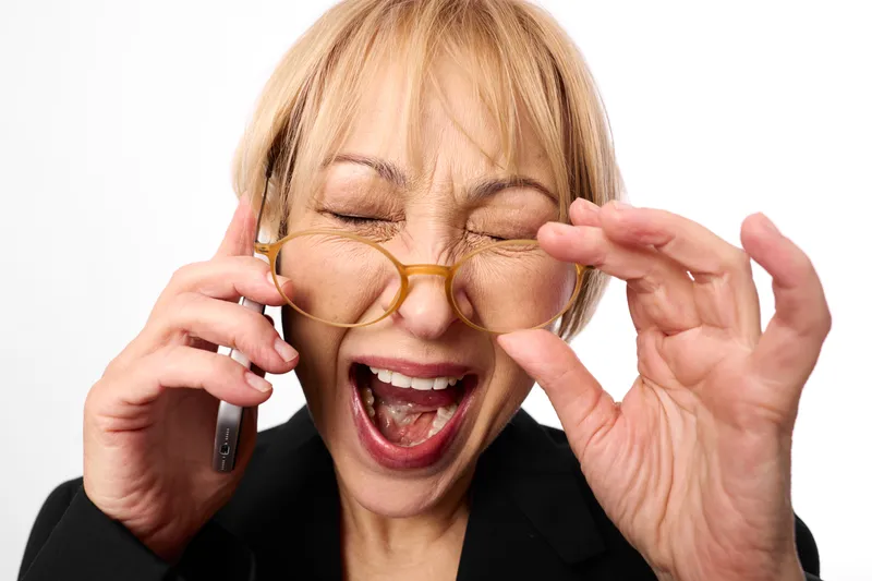 woman phone glasses blond portrait closeup laughing funny business stress, blond woman black blazer holds smartphone to ear, eyeglasses, open mouth reaction, bright white background